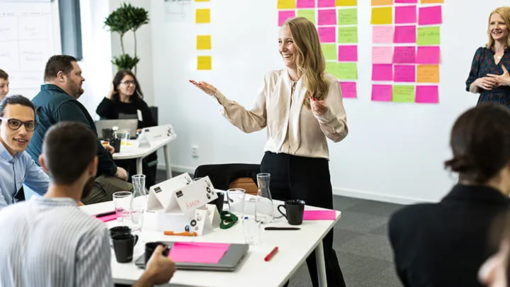 Facilitator leading an interactive workshop at Trelleborg Group University, with participants seated at tables discussing ideas and colorful notes on the wall behind them.