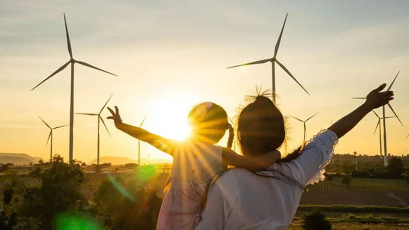 Adult and child overlooking wind turbines at sunset, representing renewable energy and climate action.