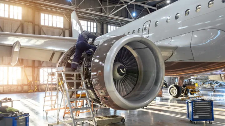 Aircraft engine maintenance in a hangar with a technician working on the engine using a ladder