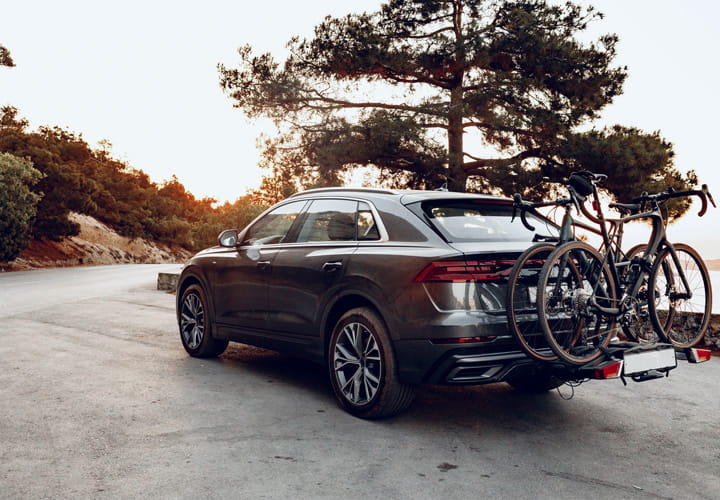 SUV sombre garé sur une route panoramique au coucher du soleil avec deux vélos fixés sur un porte-vélos arrière