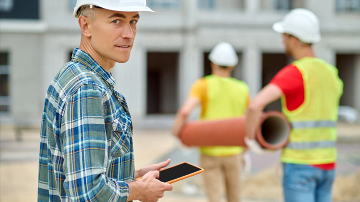Byggarbetare som hanterar rör på plats, med en person som håller en surfplatta