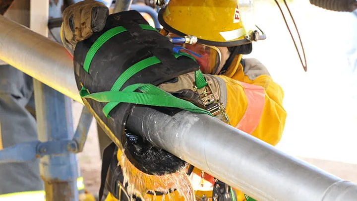 A man wearing protective equipment fixing a pipe that conveys hazardous materials