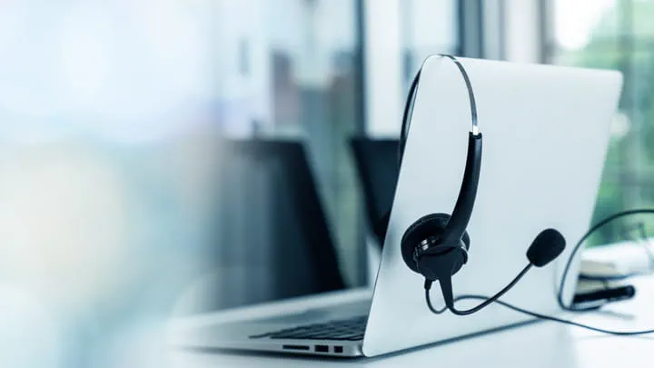 A laptop with headphones hanging from the screen, representing customer service